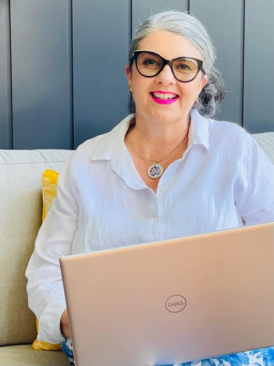 A woman in glasses sitting on a couch with a laptop.